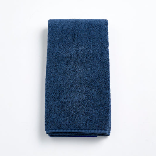 Folded indigo blue hand towel made of soft, textured cotton terry cloth on a white background.