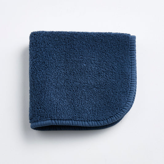 Indigo blue Signature washcloth in soft, textured cotton terry with a rounded corner and finished fabric trim.