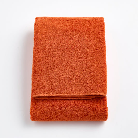 Folded pumpkin orange Signature bath towel made of plush, absorbent cotton terry fabric.