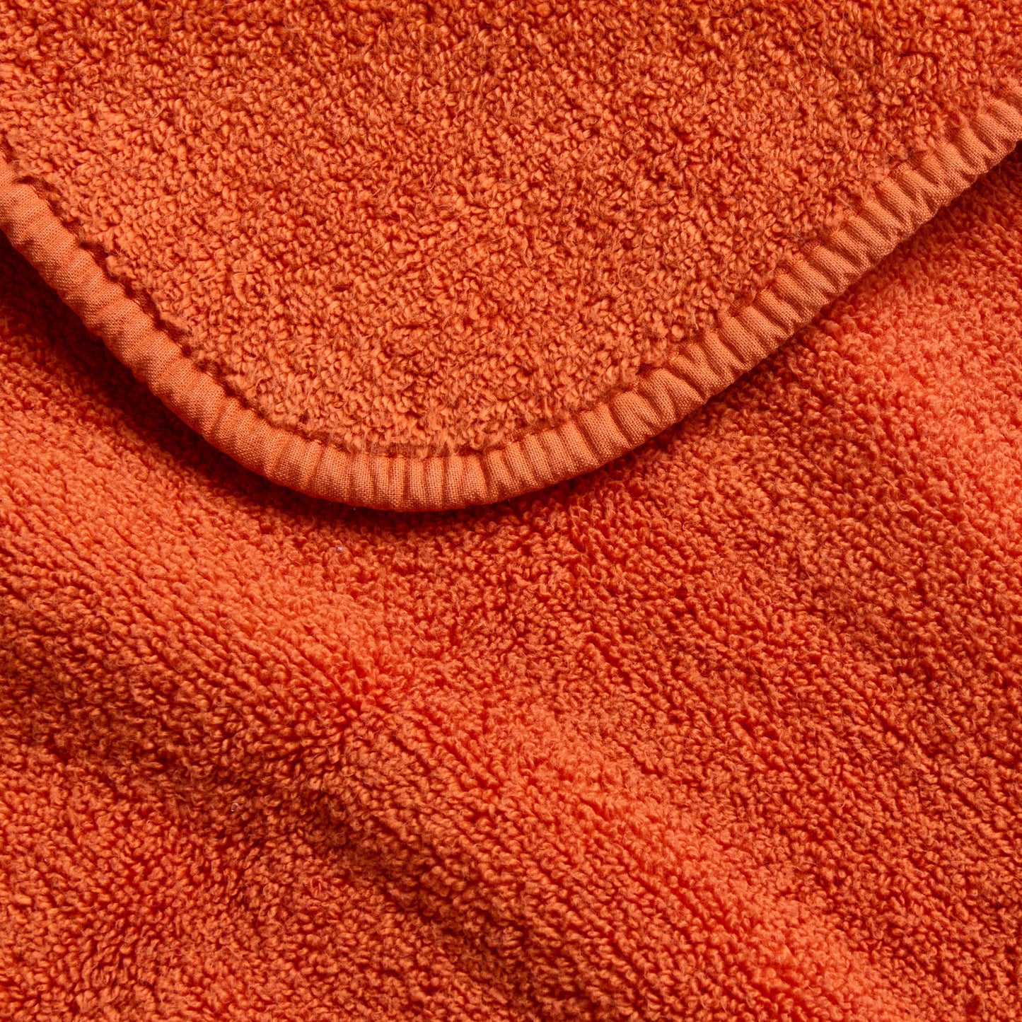 Close-up of a plush, pumpkin-orange cotton bath towel featuring a soft terry texture and a finished stitched edge.