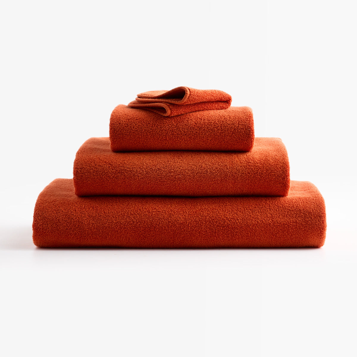 Stacked pumpkin orange HG Signature zero-twist cotton bath towels with piped edges on a white background.
