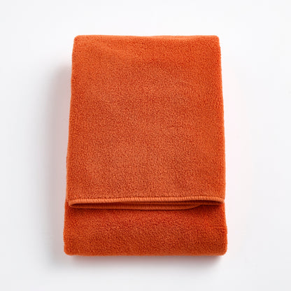 Folded pumpkin orange Signature bath towel made of plush, absorbent cotton terry fabric.