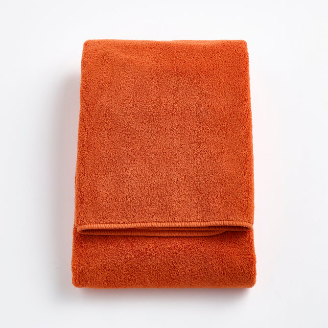 Folded pumpkin orange Signature bath towel made of plush, absorbent cotton terry fabric.