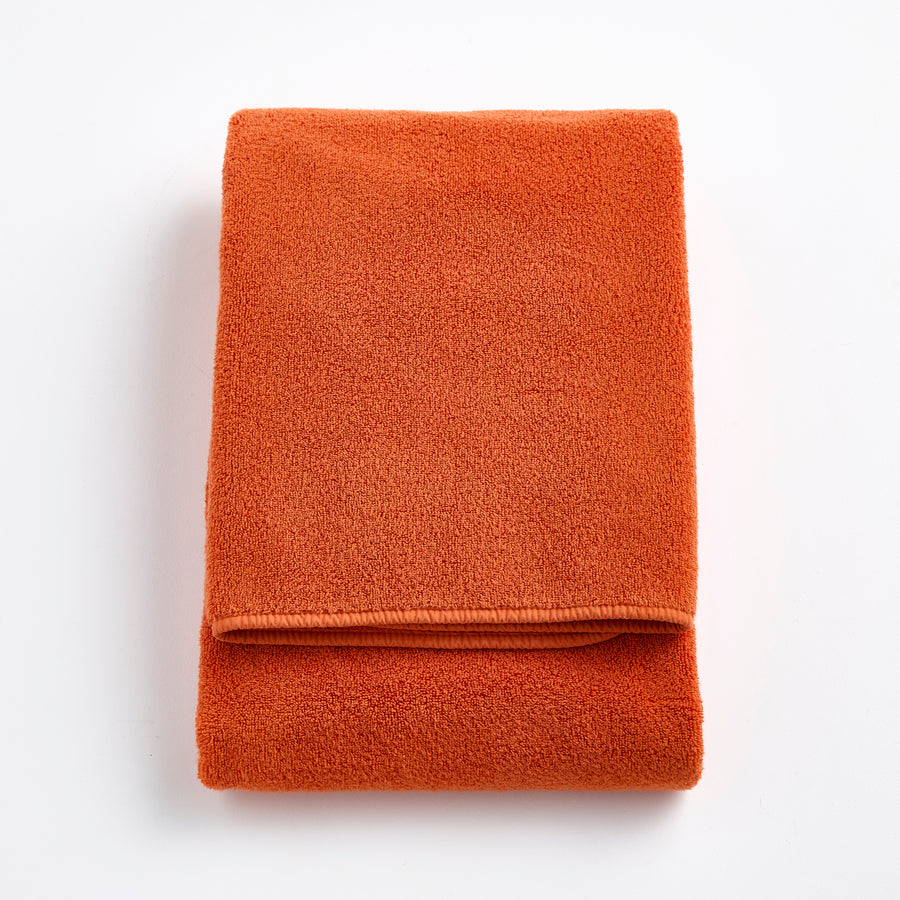 Folded pumpkin orange Signature bath towel made of plush, absorbent cotton terry fabric.