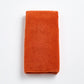 Folded pumpkin orange Signature hand towel made of soft, textured cotton terry cloth on a white background.