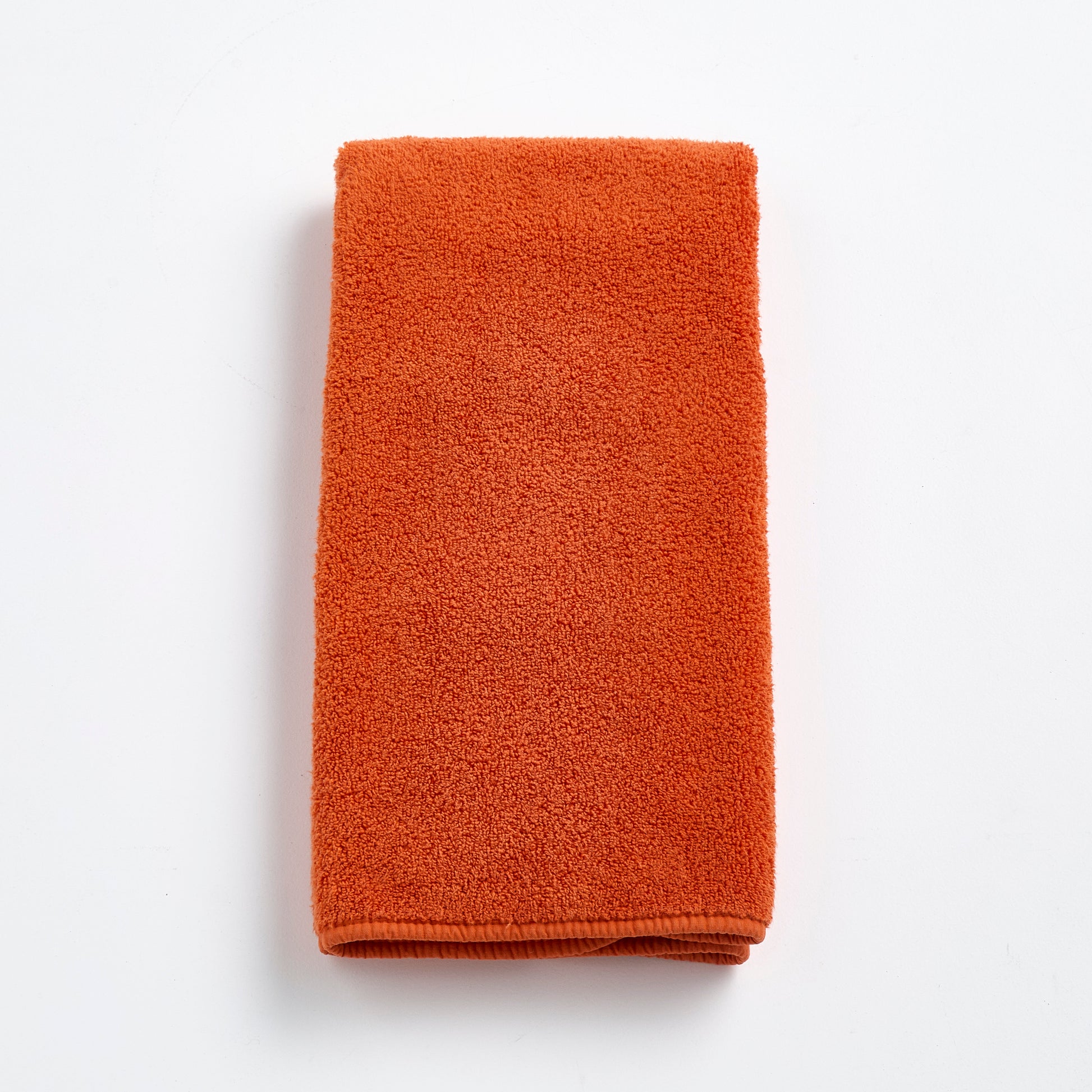 Folded pumpkin orange Signature hand towel made of soft, textured cotton terry cloth on a white background.