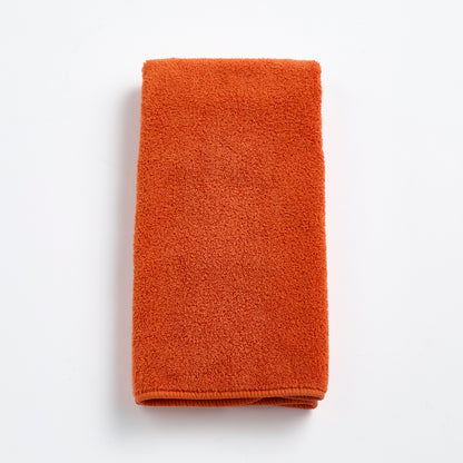 Folded pumpkin orange Signature hand towel made of soft, textured cotton terry cloth on a white background.