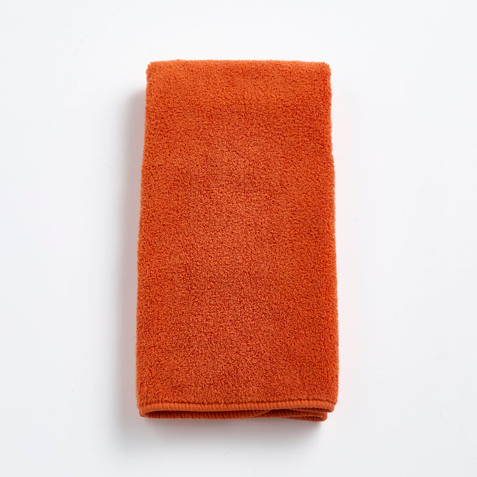 Folded pumpkin orange Signature hand towel made of soft, textured cotton terry cloth on a white background.