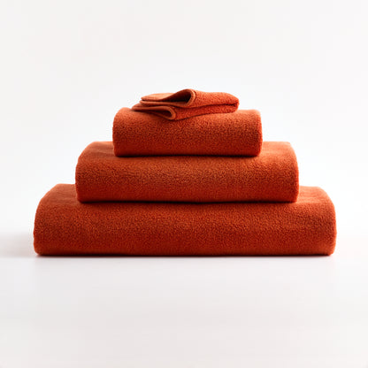 Stack of soft pumpkin orange zero-twist cotton washcloths and towels with piped edges on a white background.