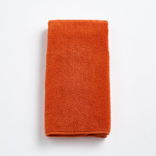 Folded pumpkin orange Signature hand towel made of soft, textured cotton terry cloth on a white background.