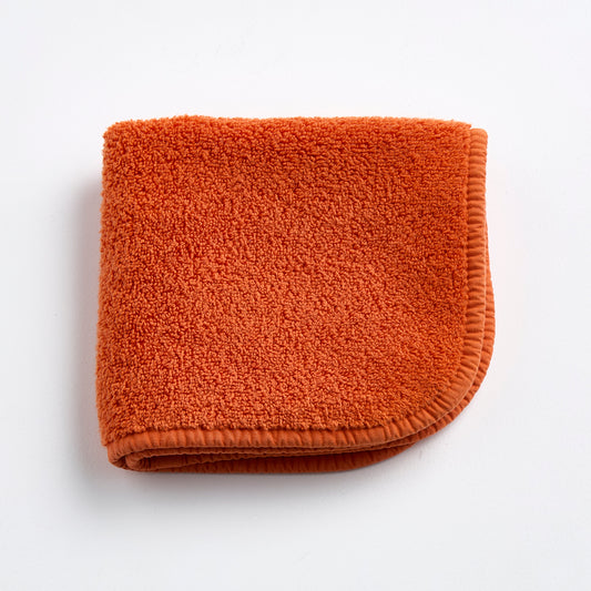 Folded pumpkin orange cotton terry washcloth with a finished stitched edge on a white background.