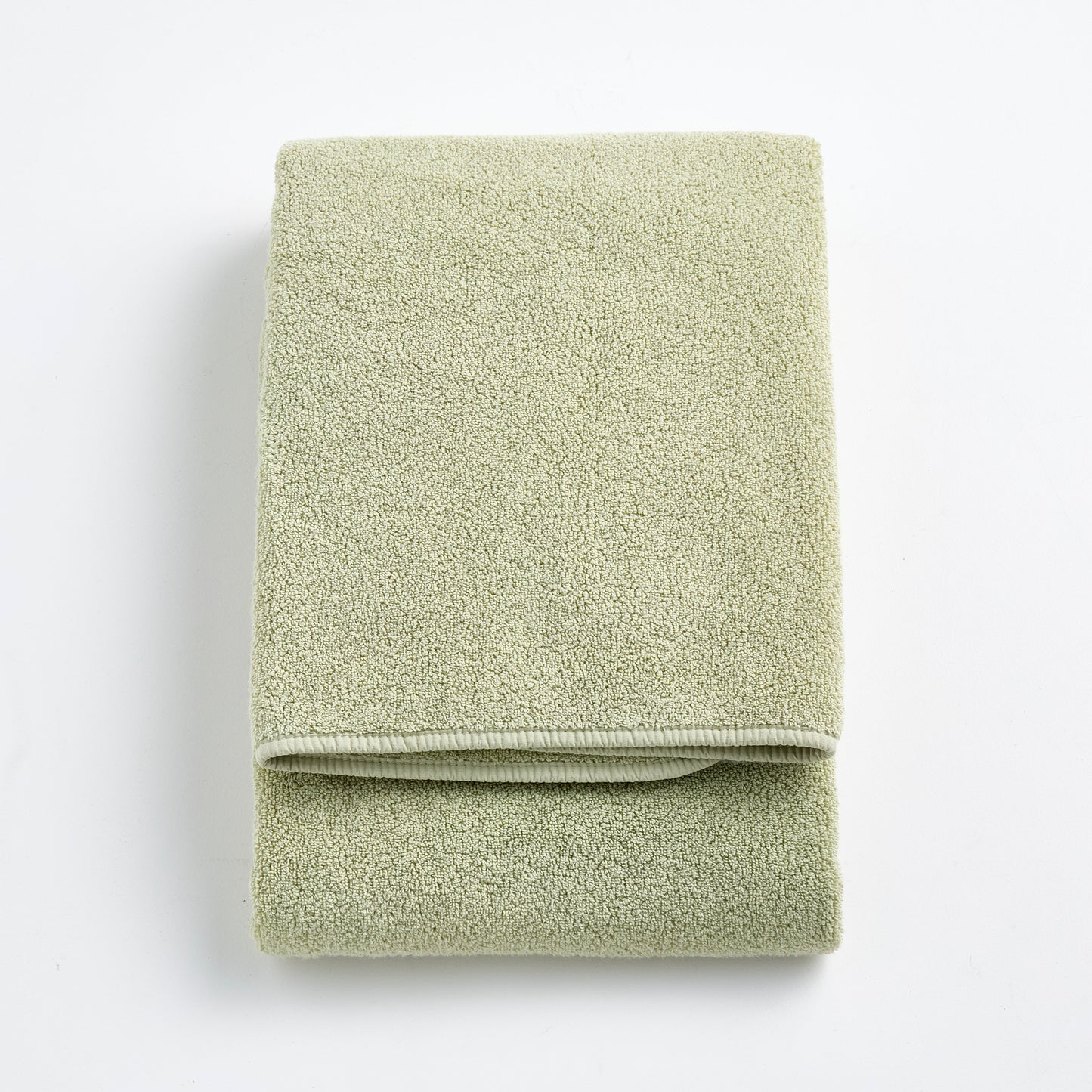 Folded sage green Signature bath towel made of soft, textured cotton terry fabric on a white background.