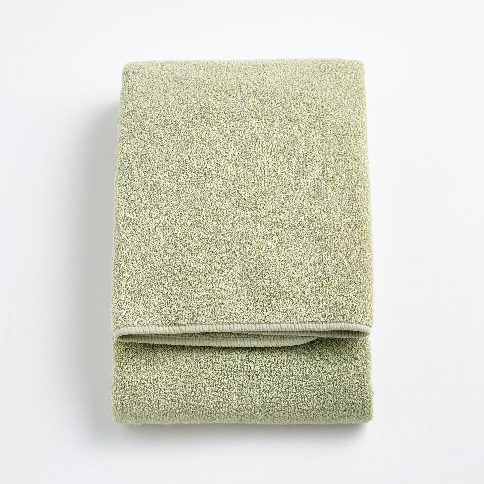 Folded sage green Signature bath towel made of soft, textured cotton terry fabric on a white background.