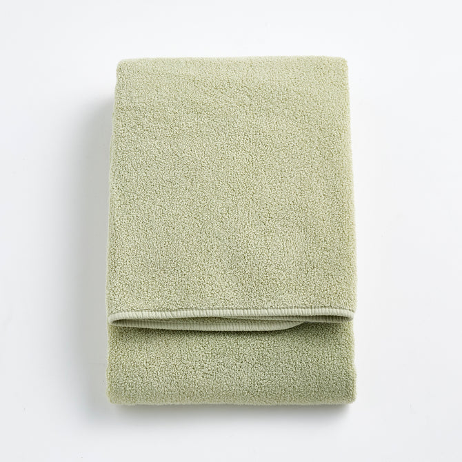 Folded sage green Signature bath towel made of soft, textured cotton terry fabric on a white background.