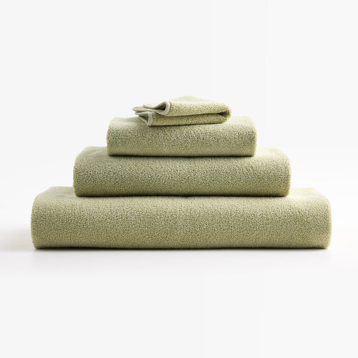Stacked sage green HG Signature zero-twist cotton hand towels with piped edges on a white background.