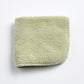 Sage green cotton washcloth with a textured loop pile and a finished stitched border.
