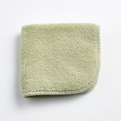 Sage green cotton washcloth with a textured loop pile and a finished stitched border.