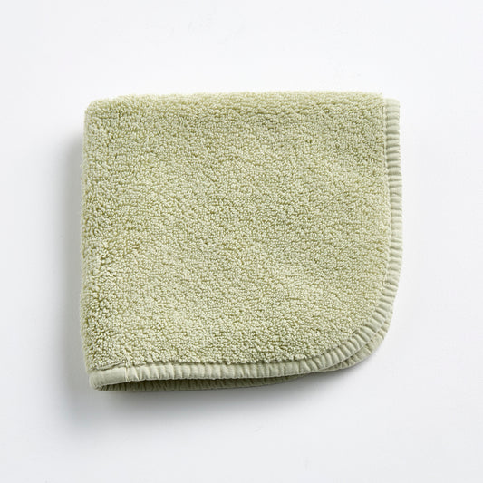 Sage green cotton washcloth with a textured loop pile and a finished stitched border.