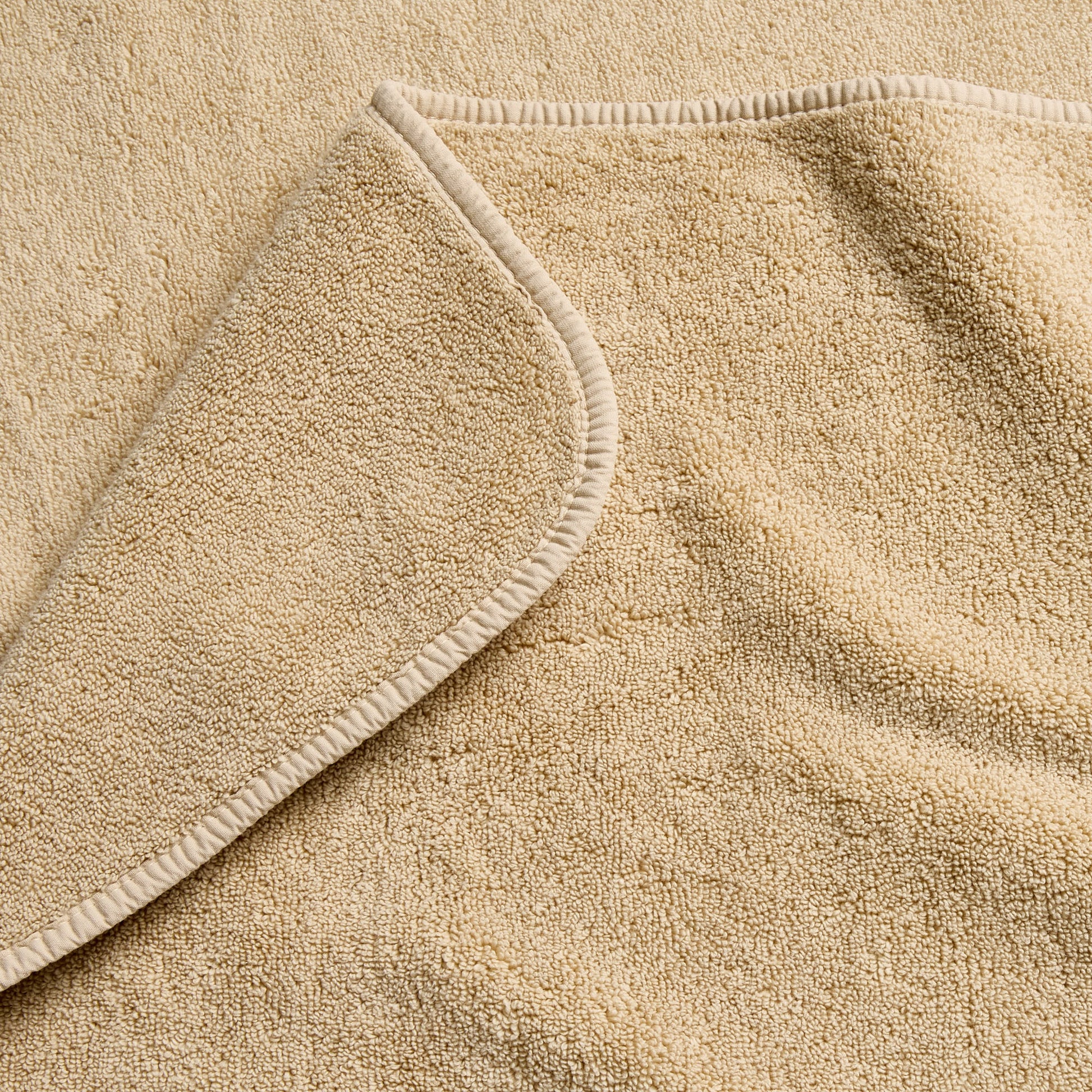 Sand-colored Signature bath sheet in plush, absorbent cotton terry fabric with a finished hemmed edge.