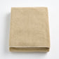 Folded sand-colored Signature bath sheet in plush, absorbent cotton terry fabric with a clean hemmed edge.