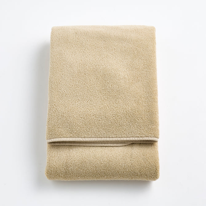 Folded sand-colored Signature bath towel in plush, high-quality cotton terry fabric with a clean hemmed edge.