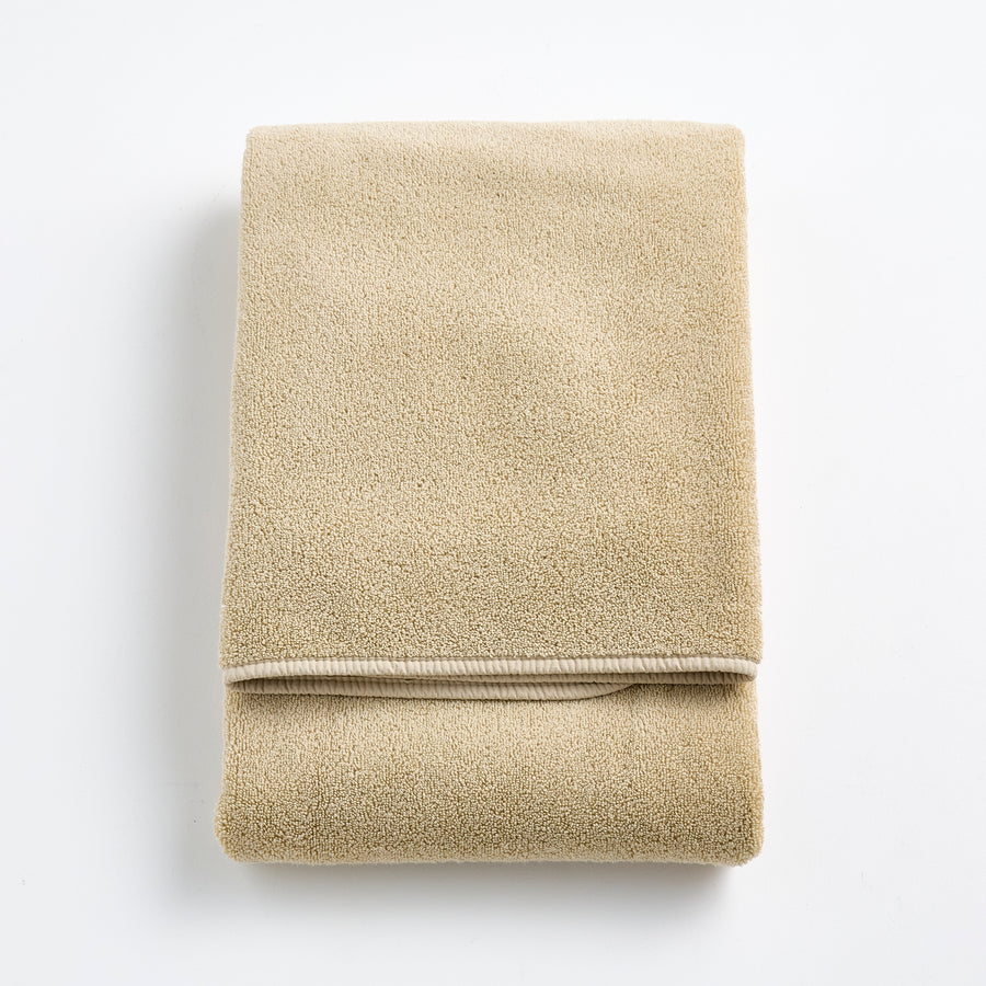 Folded sand-colored Signature bath towel in plush, high-quality cotton terry fabric with a clean hemmed edge.