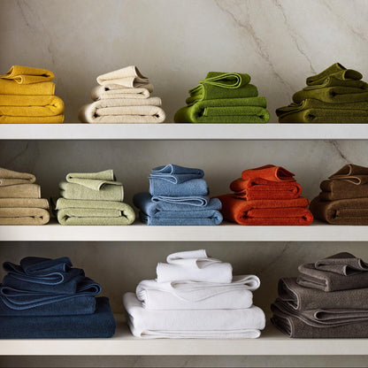 Stacks of HG Signature zero-twist cotton hand towels in various colors arranged on white shelves.