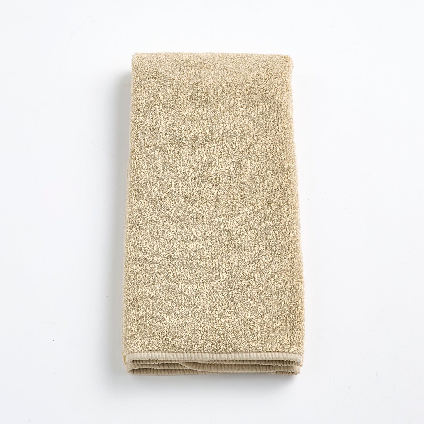 Folded sand-colored Signature hand towel made of plush, absorbent cotton terry fabric on a white background.