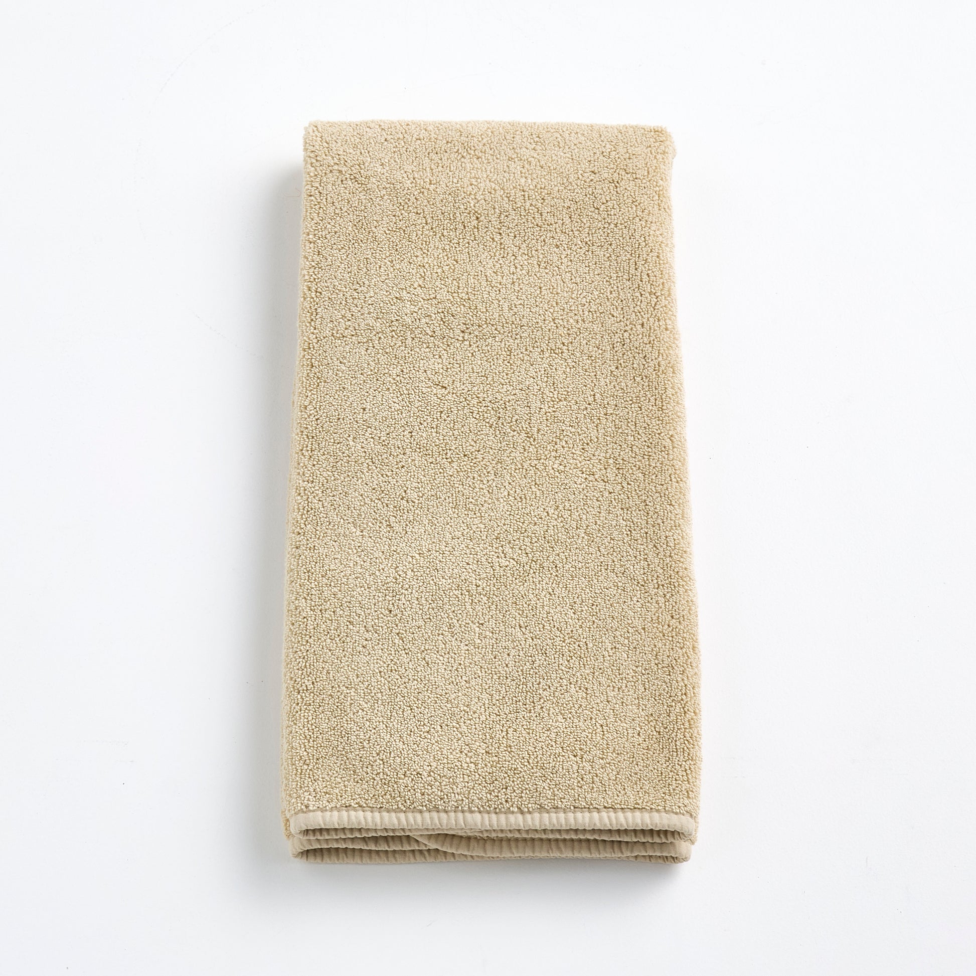 Folded sand-colored Signature hand towel made of plush, absorbent cotton terry fabric on a white background.