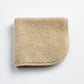 Folded sand-colored Signature washcloth in plush cotton terry with a rounded corner and stitched hem.