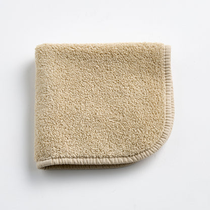 Folded sand-colored Signature washcloth in plush cotton terry with a rounded corner and stitched hem.