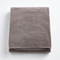 Folded stone gray bath sheet made of plush, absorbent cotton terry fabric with a clean hemmed edge.