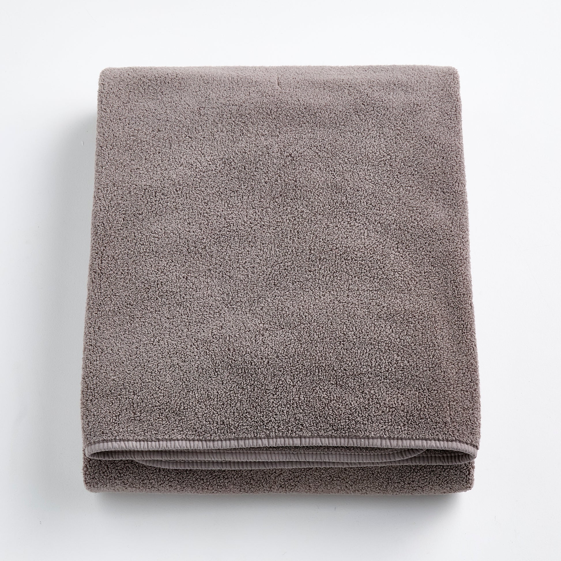 Folded stone gray bath sheet made of plush, absorbent cotton terry fabric with a clean hemmed edge.
