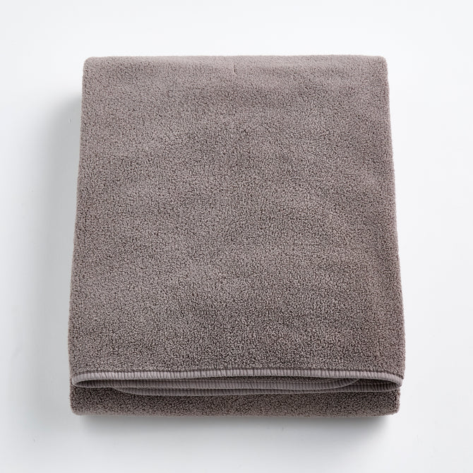 Folded stone gray bath sheet made of plush, absorbent cotton terry fabric with a clean hemmed edge.