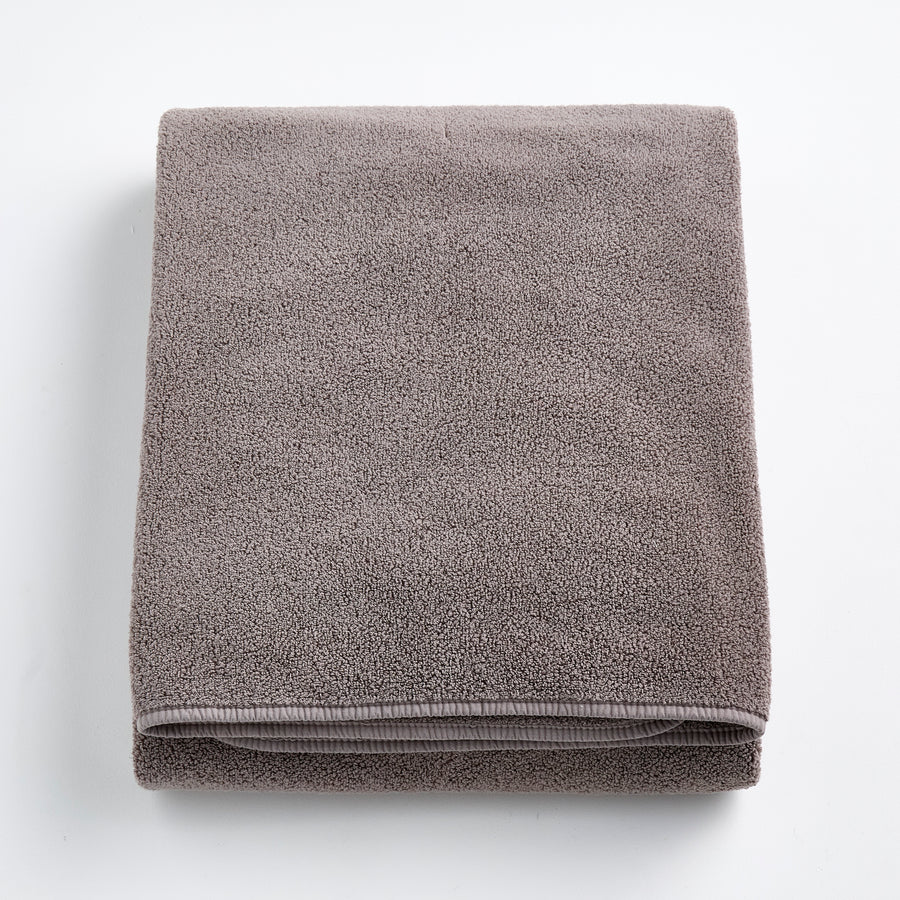 Folded stone gray bath sheet made of plush, absorbent cotton terry fabric with a clean hemmed edge.