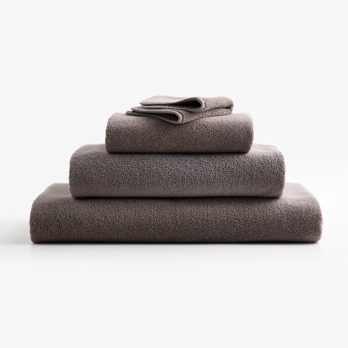 Stack of stone gray HG Signature zero-twist cotton bath towels with piped edges on a white background.