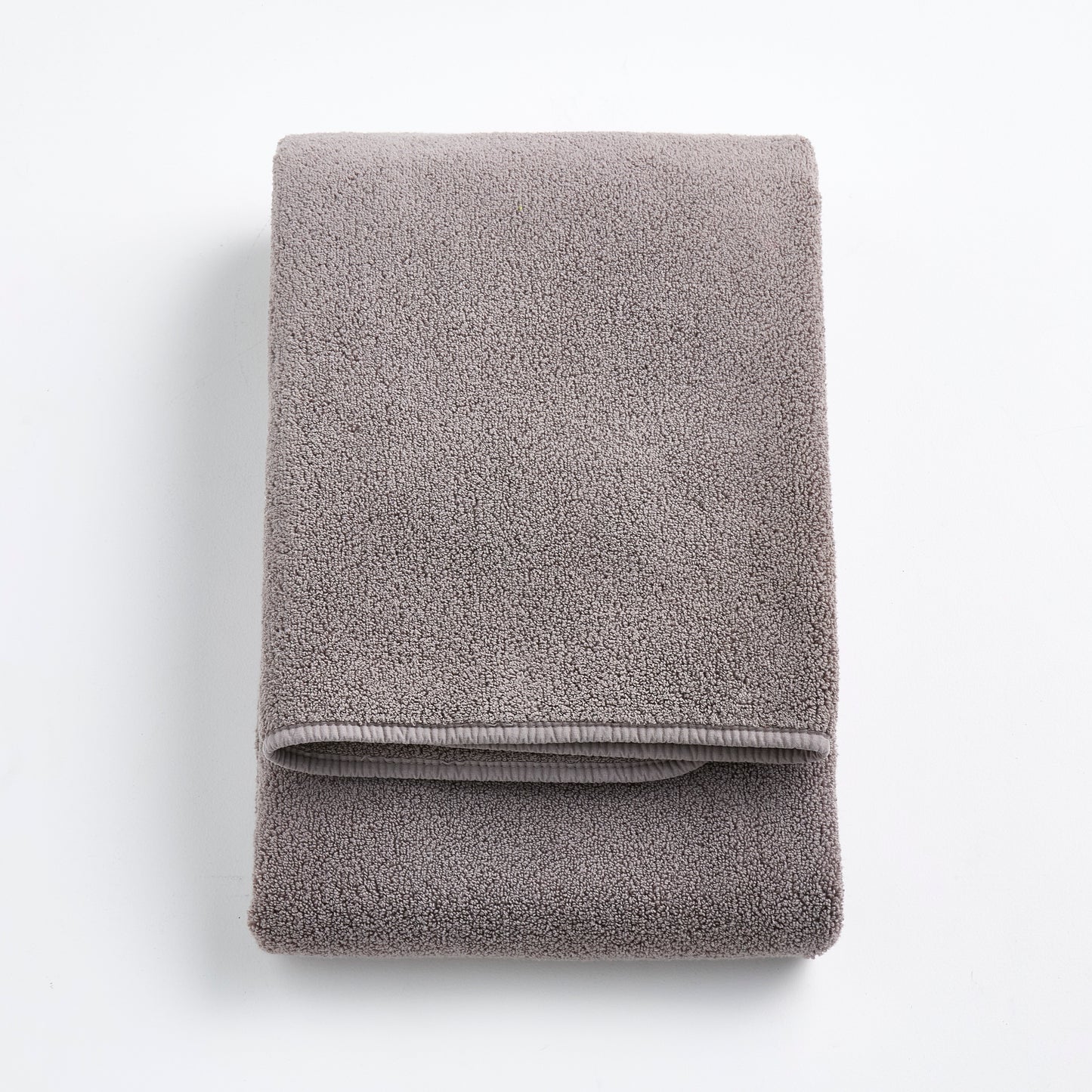 Folded stone gray Signature bath towel in plush, high-quality cotton terry fabric on a white background.