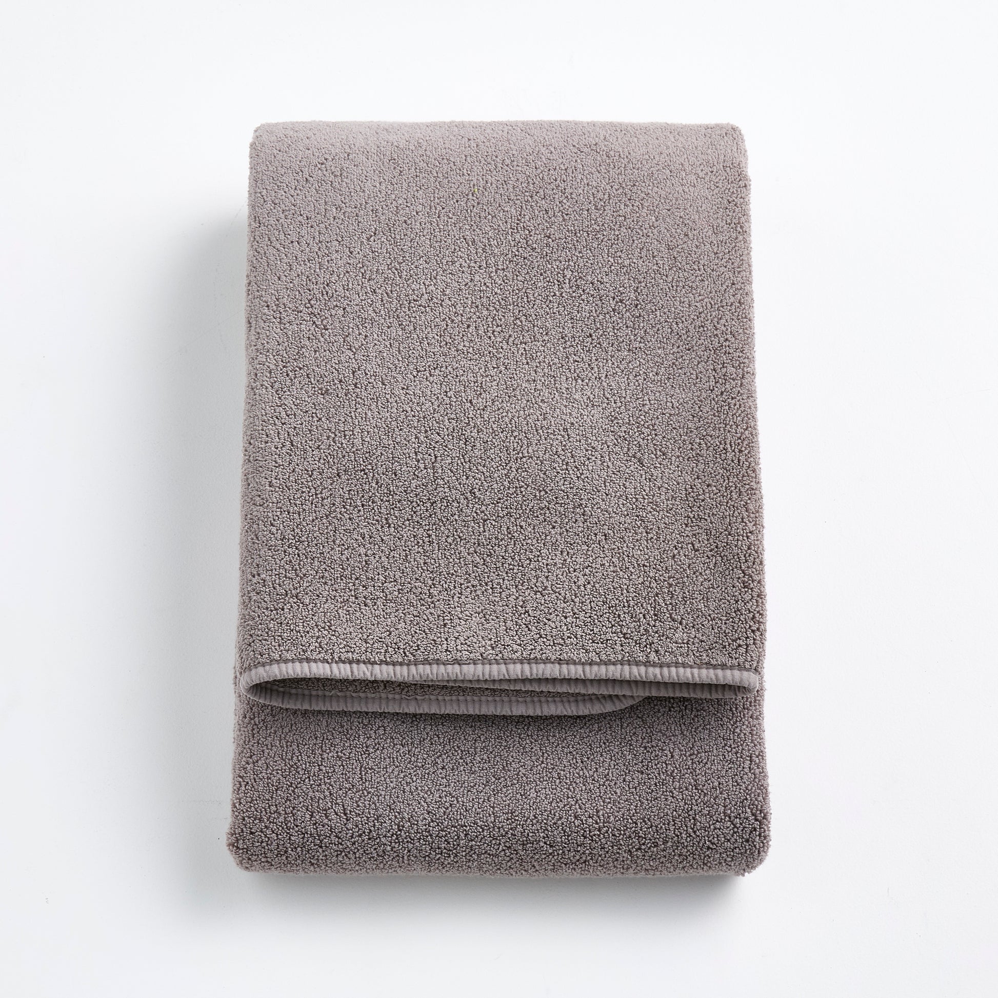 Folded stone gray Signature bath towel in plush, high-quality cotton terry fabric on a white background.
