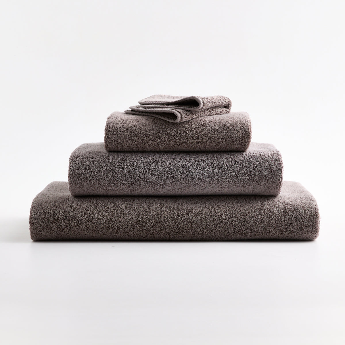 Stacked stone gray HG Signature zero-twist cotton washcloths and towels with piped edges.
