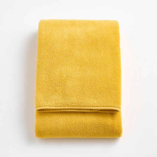 Folded bright yellow Signature bath towel made of soft, plush cotton terry fabric on a white background.