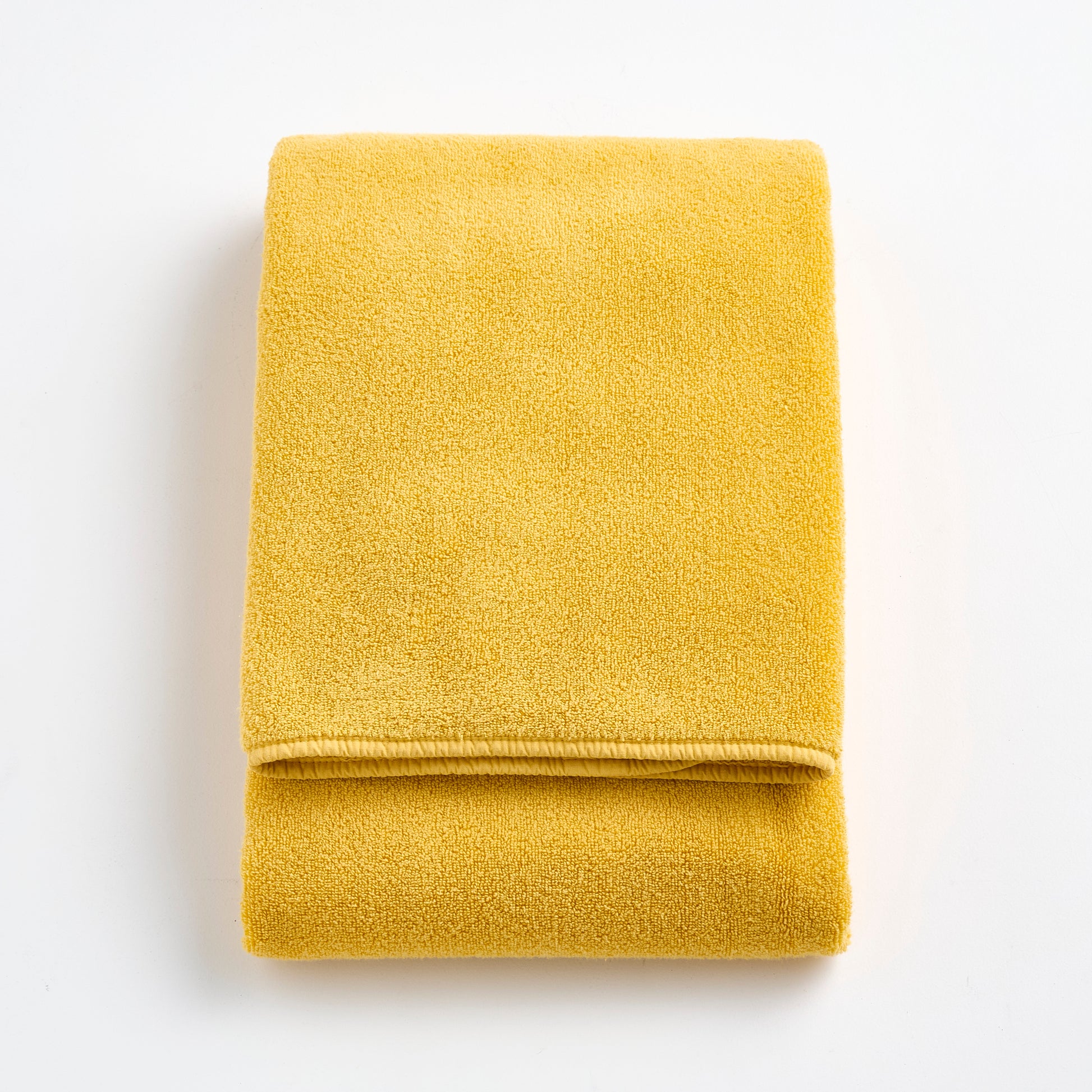 Folded bright yellow Signature bath towel made of soft, plush cotton terry fabric on a white background.