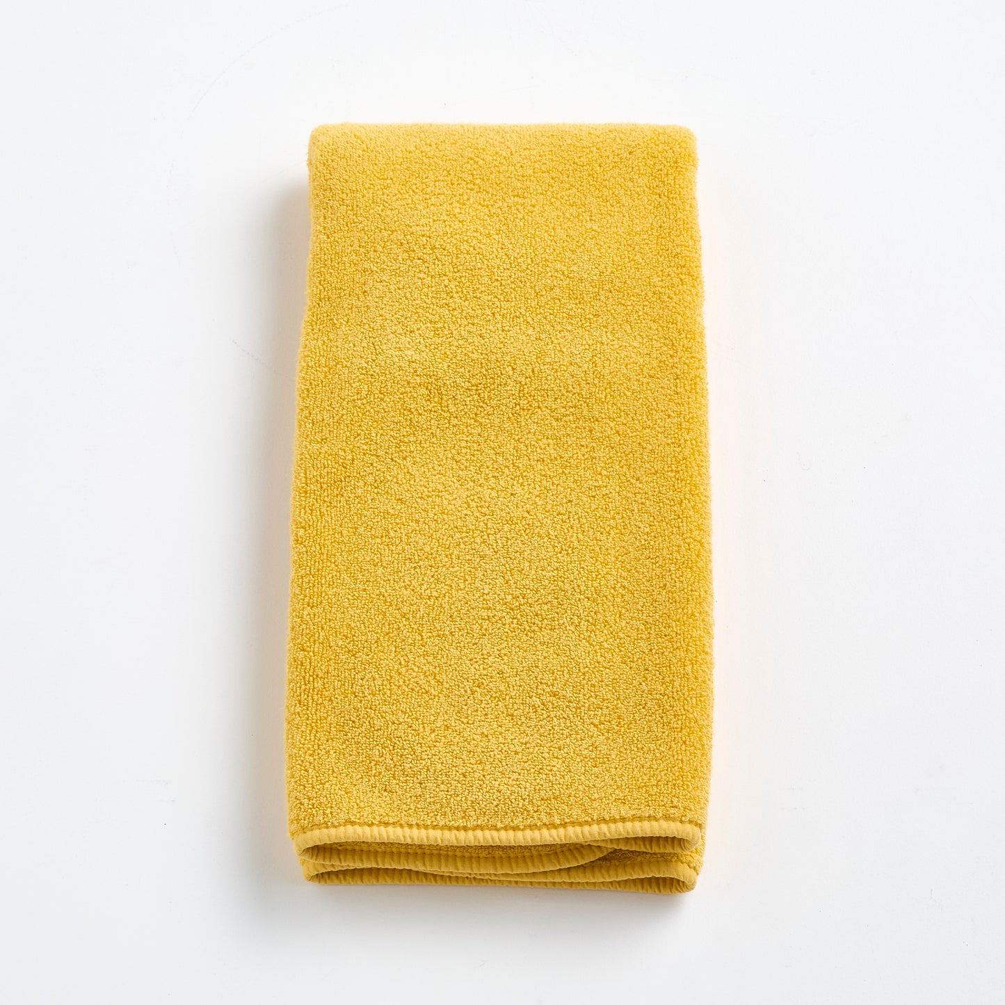 Folded bright yellow Signature hand towel made of soft, textured cotton fabric on a white background.