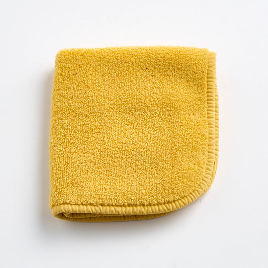 Folded yellow cotton terry washcloth with a stitched border on a white background.
