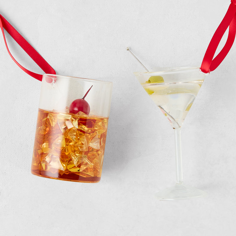 Manhattan and martini glass Christmas ornaments with red ribbon hangers on a white background.