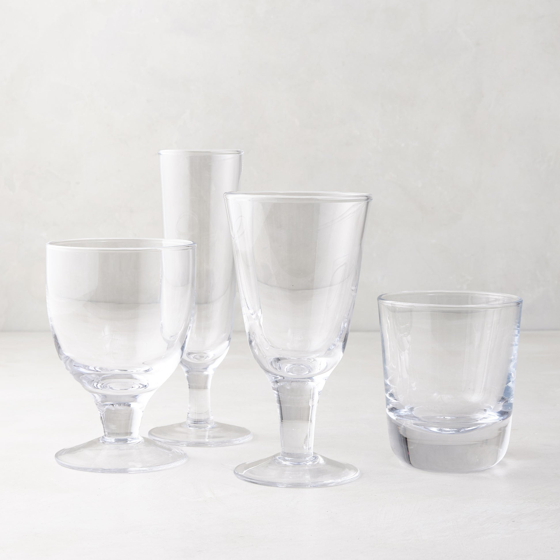 Four clear glass Hudson and Henri style drinkware pieces: a champagne flute, two stemmed glasses, and a tumbler.