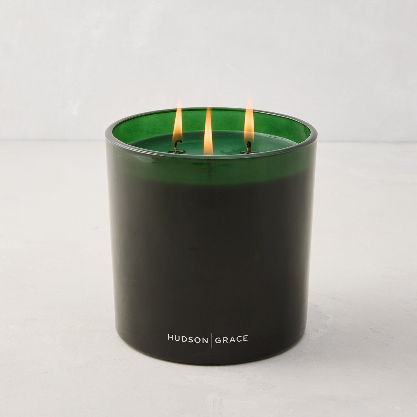 Hudson Grace Aspen Scented 3-Wick Candle in a dark green glass vessel with three lit wicks.
