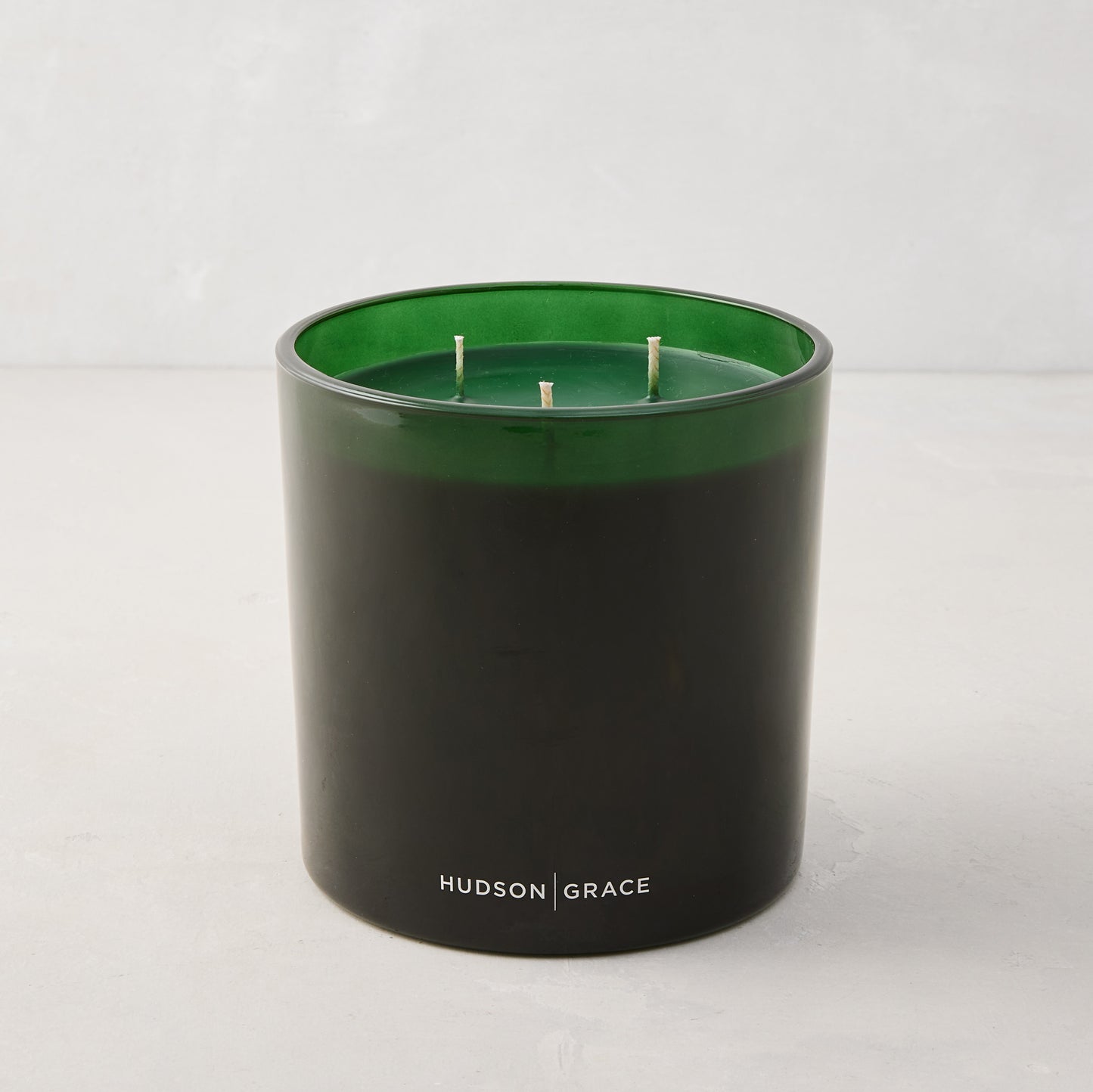 Hudson Grace Aspen Scented 3-Wick Candle in a dark green glass vessel with white logo.