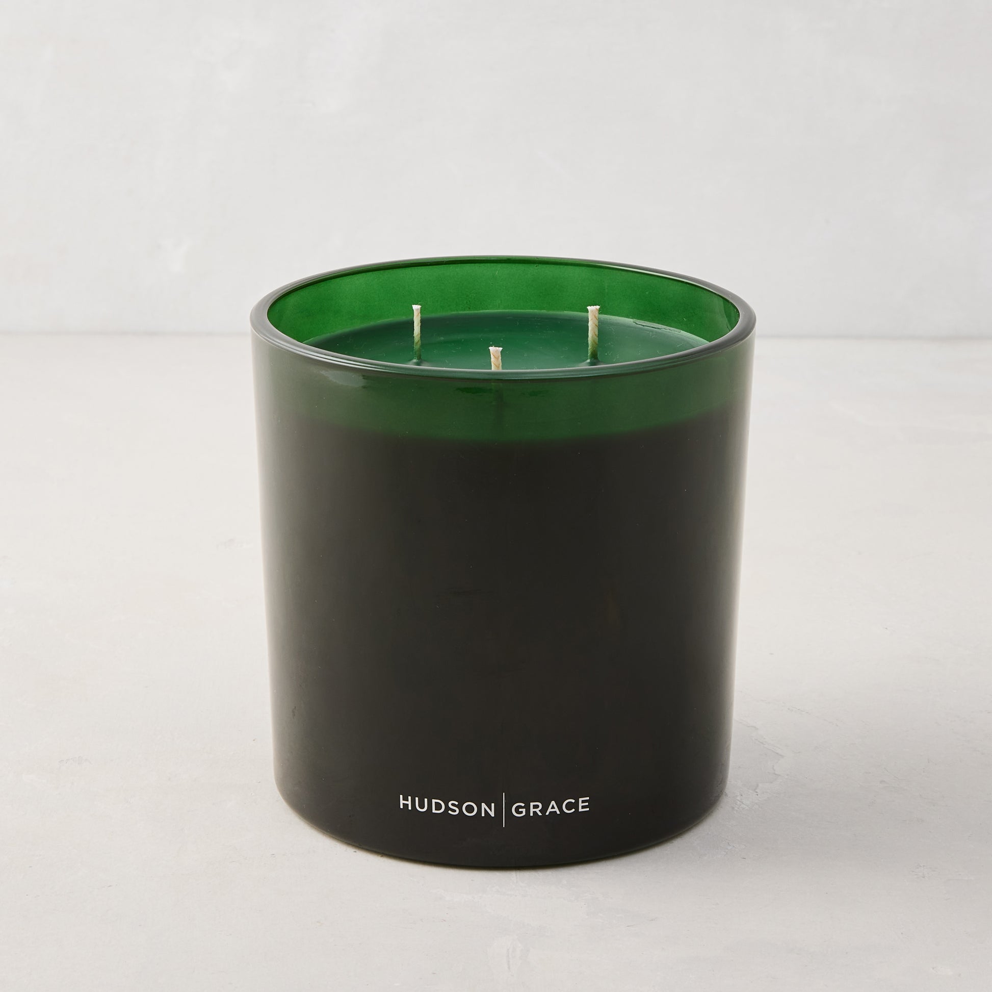 Hudson Grace Aspen Scented 3-Wick Candle in a dark green glass vessel with white logo.