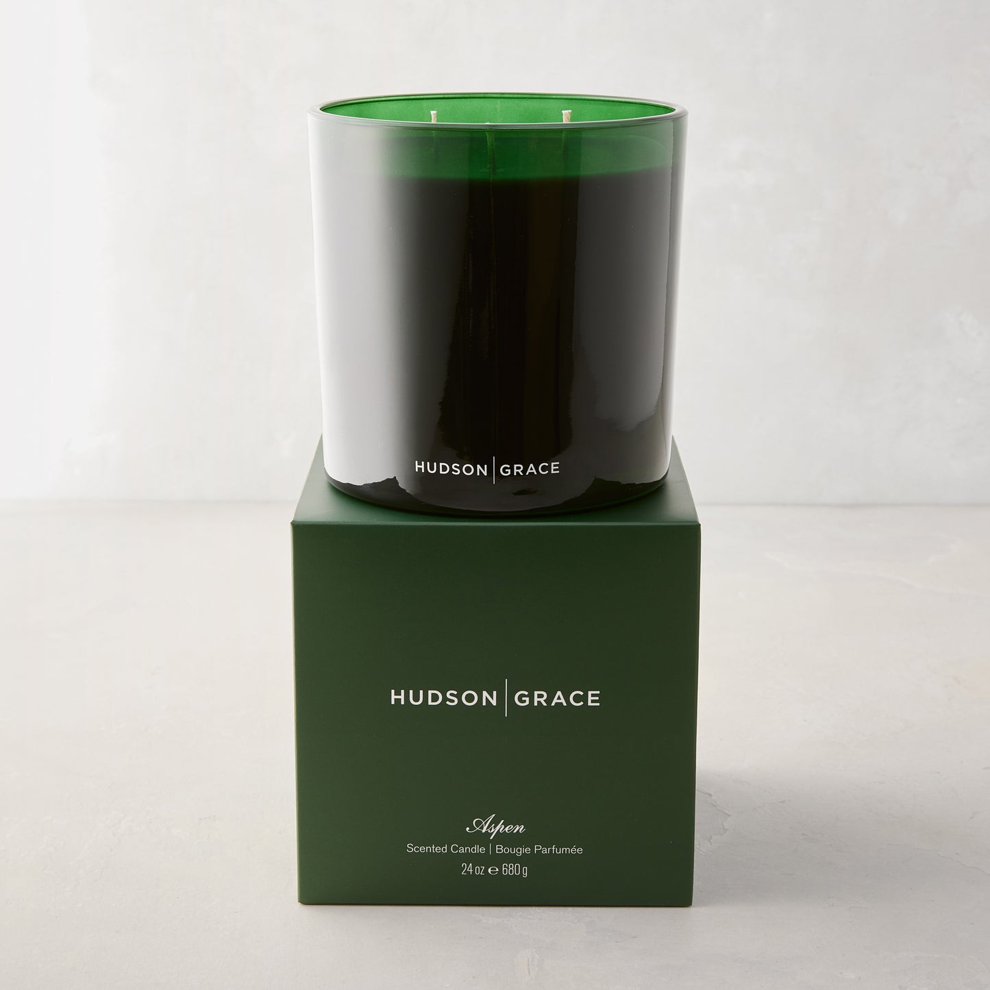 Hudson Grace Aspen 3-wick candle in a dark green glass vessel, atop a matching green gift box.