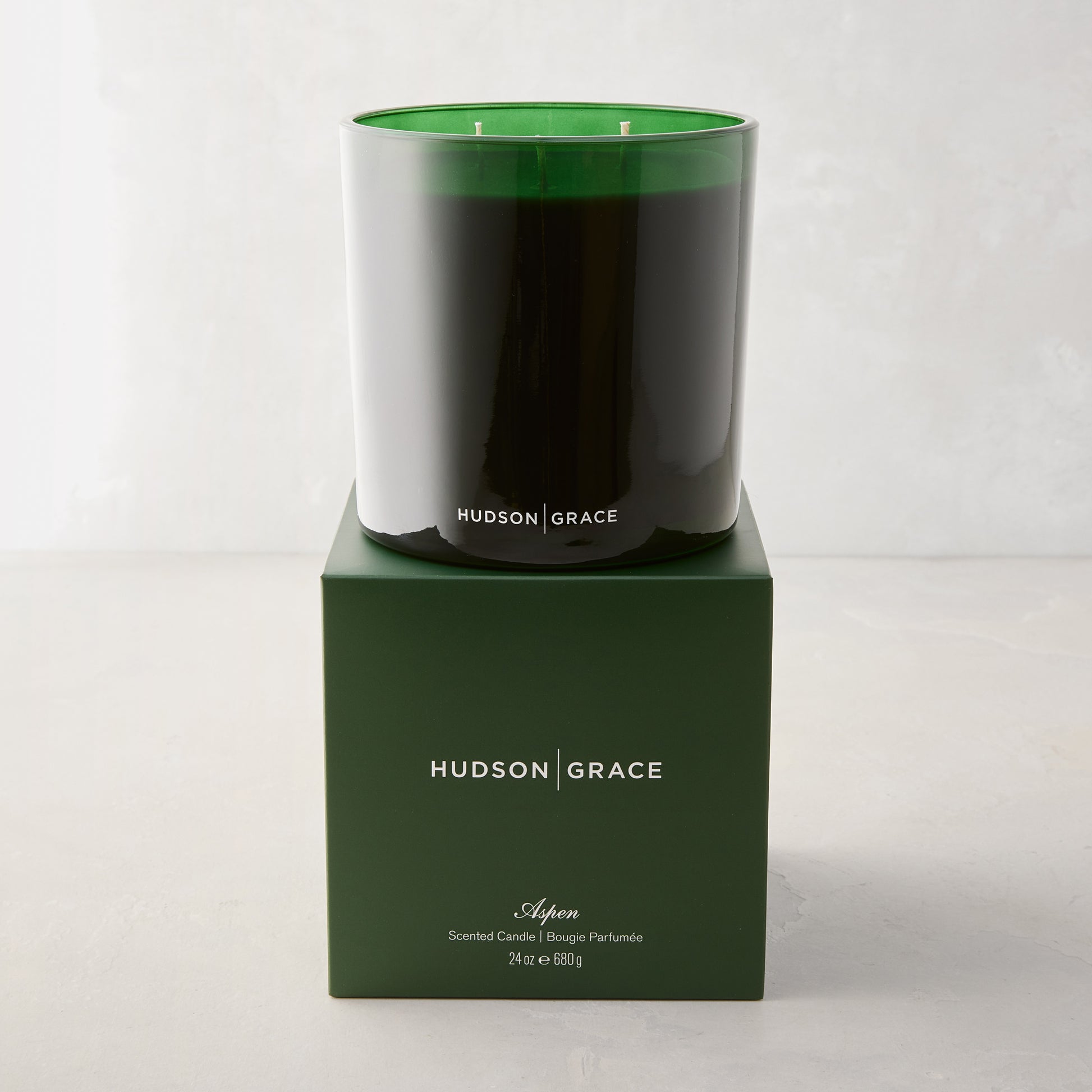 Hudson Grace Aspen 3-wick candle in a dark green glass vessel, atop a matching green gift box.